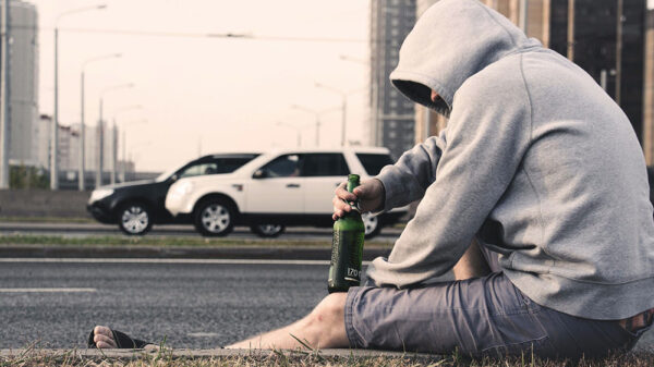 man wearing hoodie sitting on the gutter holding a bottle of wine